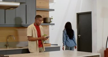 Akıllı telefonları kaydırıyor, Afro-Amerikan çift yemek için yemek çubuklarını adada açıyor. Teknoloji, samimiyet, iletişim, yemek, yaşam tarzı, modern, samimi