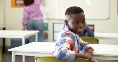 Sınıfta gülümseyen Afrikalı Amerikalı çocuk, okulda bayan öğretmen yazarken kameraya bakıyor. eğitim, öğrenim, okul, öğrenci, akademik, gençlik