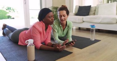 Çeşitli bayan arkadaşlar akıllı telefon istemlerine tepki veriyor, uygulamaları kullanıyor ve yoga minderleri üzerinde egzersiz yapıyorlar. Sağlık, dostluk, motivasyon, dijital fitness, gündelik, modern, sağlıklı yaşam