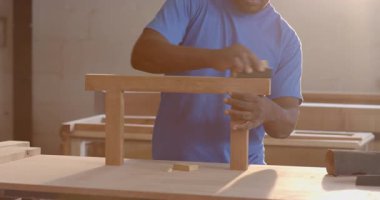 Afrika kökenli Amerikalı erkek iş arkadaşları atölyede zımpara bloğu ve gözlüklerle odun zımparalıyorlar. Sanatçılık, takım çalışması, atölye, yenilik, kırsal, beceri, işbirliği