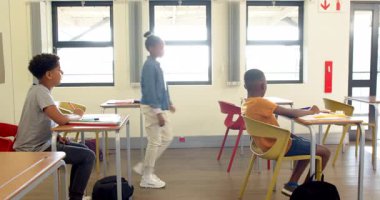 Sınıftaki çok ırklı öğrenciler okul grup aktiviteleri sırasında sohbet edip gülümsüyorlar. Sınıf arkadaşları, takım çalışması, işbirliği, eğitim, tartışma, öğrenme