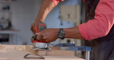 Önlük takan kıdemli Afro-Amerikalı bir adamı zımparalanmış tahtayla tezgaha kelepçelemek. Marangozluk, marangozluk, ahşap işçiliği, atölye, işçilik, marangozluk, mobilya, diy