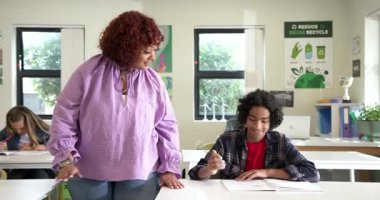 Okulda, bayan öğretmen çocuğa ödevlerinde yardım ediyor, öğrenme ve bağlanmayı teşvik ediyor. Eğitim, öğretim, sınıf, akıl hocası, akademik, öğretim