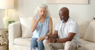 Beyaz hap şişesi almak, yaşlı çiftler hapları doldurmak, içme suyu içmek, kanepede sağlığa kadeh kaldırmak. Yaşlılık, arkadaşlık, sağlık, ilaç, rahatlama, konfor, bakım