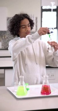 Dikey video: Fen sınıfındaki öğrenci laboratuvar şişesinde renkli sıvılarla deney yapıyor. kimya, eğitim, araştırma, okul, öğrenim, keşif