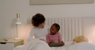 Çeşitli anne ve kız tableti yatakta açıyor, ekrana dokunuyor, araklıyor ve hikayeyi keşfediyor. Aile, bağ, eğitim, dijital öğrenme, çocukluk, ev, teknoloji