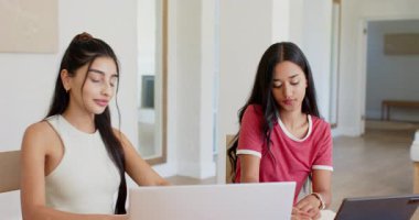 Masada oturan, dizüstü bilgisayarda el kol hareketi yapan, kalemle tablet yazan kız arkadaşlar. İşbirliği, arkadaşlık, dijital, çalışma alanı, iletişim, üretkenlik, modern