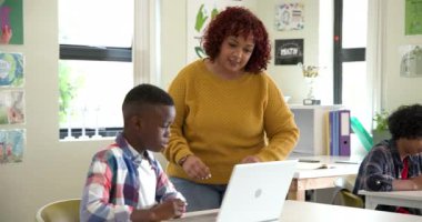 Bayan öğretmen, Afrika kökenli Amerikalı çocuğa sınıfta dizüstü bilgisayarıyla yardım ediyor, okulda öğrenmeye odaklanıyor. eğitim, akıl hocalığı, teknoloji, takım çalışması, öğretim, dijital öğrenme