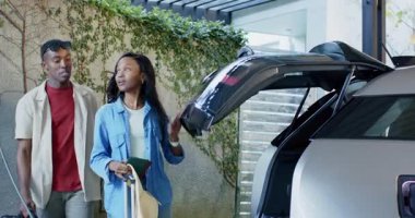 Afro-Amerikalı bir çift garaj kapısına gelip valizleri şarj kablosuyla birlikte SUV bagajına yüklüyorlar. Elektrik, seyahat, macera, modern, açık hava, yaşam tarzı, teknoloji