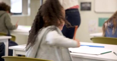 Sınıfta gülümseyen kız deftere yazı yazıyor, okul aktivitelerinden zevk alıyor. Öğrenme, eğitim, mutluluk, çocukluk, öğrenim, ilkokul