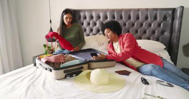 Çeşitli çiftler yataklarında bavul hazırlıyor kıyafet seçiyorlar pasaport kontrol ediyorlar ve akıllı telefonları kaydırıyorlar. Seyahat hazırlığı, paketleme, organizasyon, yaşam tarzı, tatil, boş zaman, modern