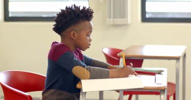 Okulda, genç Afro-Amerikan çocuk dikkatle sınıf masasında deftere yazı yazıyordu. Eğitim, öğrenim, öğrenim, konsantrasyon, çocukluk, akademik