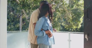 Güneş ışığı, cam balkon korkuluklarını kucaklayan Afrika kökenli Amerikalı çifti ağaçların tepelerine doğru çekiyor. Romantizm, mahremiyet, bağlantı, doğa, sükunet, boş zaman, açık hava