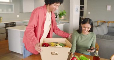 Çeşitli kutuları açan çift, biber öğütücüsünü mutfakta yemek tarifini kontrol eden kadın olarak gösteren adam. Taze ürün, ev yapımı, modern mutfak, malzeme seçimi, aşçılık, ev yemeği, yaşam tarzı.