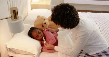 Anne, termometrede hasta siyah kız var mı diye kontrol ediyor. Teddy 'i tutuyor. Akıllı telefondan yatağın başucunda arıyor. Ebeveynlik, bakım, bakım, konfor, sağlık, evcil, hassas