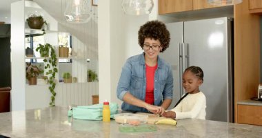 Anne kızı mutfakta yemek dilimliyor beslenme çantalarını paketliyor, okul için nane yeşili sırt çantası taşıyor. Aile, beslenme, eğitim, yetiştirme, yerli, uyum, bakım