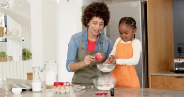 Çeşitli anne ve kız çocukları mutfak adasında kırmızı bardakla elek temizliyor ve un döküyorlar. Aile, yemek pişirme, yerli, eğitim, yaşam tarzı, sıcaklık