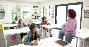 Sınıfta, çeşitli çok ırklı öğrenciler el kaldırıyor, okulda bayan öğretmenle yakınlaşıyorlar. eğitim, öğrenme, çeşitlilik, katılım, öğretim, okul