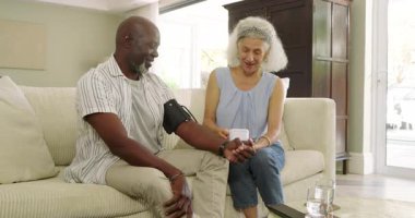 Üst düzey bir çift evde kan basıncı kelepçelerini açıyor, ölçüyor ve sağlık sonuçlarını tartışıyor. Sağlık, bakım, evcil, şefkatli, modern, ailevi, konfor.