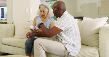 Tansiyon monitörü tutan yaşlı çift kanepenin üzerinde sağlık kontrolü için bilek ölçümü yapıyor. Sağlık, yaşlılık, sağlık, ev, teknoloji, bağlantı, yaşam tarzı