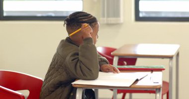 Sınıfta, not defterine yazan genç bir çocuk, ödevlerine konsantre oluyor. Eğitim, öğrenme, öğrenim, konsantrasyon, çocuk