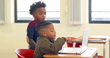 Okulda, genç Afrikalı Amerikalı çocuk dizüstü bilgisayarı işaret ederek sınıf arkadaşına ödevinde yardım ediyordu. Eğitim, takım çalışması, işbirliği, öğrenme, öğrenme, teknoloji