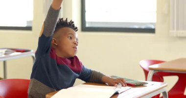 Okulda, Afrikalı Amerikalı genç bir çocuk sınıfta hevesle el kaldırıyor, katılmaya hazır. Eğitim, öğrenme, katılım, coşku, bağlılık, Afrikalı Amerikalı çocuk