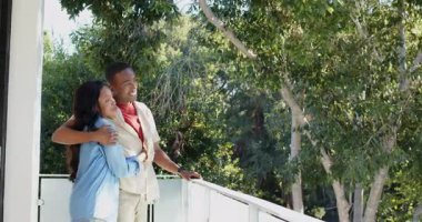 Afrika kökenli Amerikalı bir çift balkona çıkıp ağaçların tepelerine bakıyor ve korkulukları kucaklıyor. Kopya alanı. Romantik, bağlantı, doğa, rahatlık, dinginlik, açık hava, yeşillik