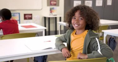 Sınıfta oturmuş gülümseyen bir öğrenci, açık bir kitapla okul gününün tadını çıkarıyor, kopya alanı. Eğitim, öğrenim, akademi, mutluluk, öğrenme, neşeli