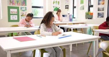 Okulda not defterine yazan gülümseyen kız, sınıf aktivitelerinin keyfini çıkarıyor. Eğitim, öğrenme, çocukluk, okula dönüş, kalem, öğrenim