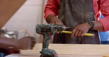 Afrika kökenli Amerikalı bir adam tezgahta tahta deliyor koruyucu önlük ve kol saati takıyor. Zanaatkar, zanaatkar, el yapımı, esnaf, marangozluk, geleneksel