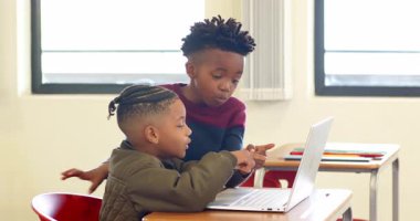 Okulda, sınıfta gülümseyen ve dizüstü bilgisayar kullanan iki çok ırklı çocuk öğrenmenin tadını çıkarıyordu. Eğitim, teknoloji, dijital, çok ırklı çocuklar, arkadaşlık, işbirliği