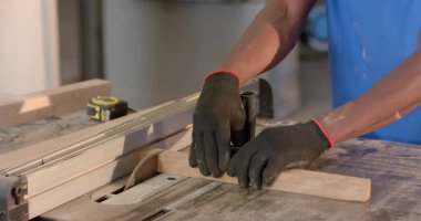 Afro-Amerikalı bir adam tezgahtaki tahta testereye rehberlik ediyor, eldiven takıyor, fotokopi çekiyor. Marangozluk, marangozluk, işçilik, atölye, alet kemeri, inşaat