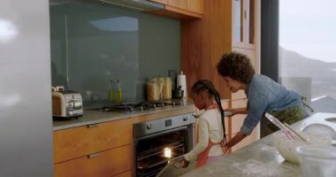 İspanyol anne, Afrika kökenli Amerikalı kızı tezgahta kek tenekesini fırına atıp dans ettiriyor. Aile, bağ, kutlama, sıcaklık, ev, gelenek, neşe