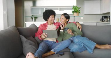 Gri kanepedeki çeşitli çiftler tablet okutma kartından beşlik çakmayı onaylıyorlar. Romantik, bağlantı, kutlama, modern, rahat, teknoloji, neşe