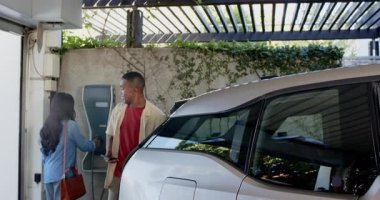 Afrika kökenli Amerikalı çift EV kablosunu çektikten sonra telefonları kontrol edip selfie çektiler. Sürdürülebilirlik, teknoloji, çevre, kentsel yaşam tarzı, çevre dostu, modern tasarım, arkadaşlık