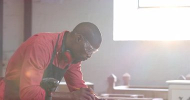 Afrika kökenli Amerikalı iş arkadaşlarının atölyede ahşap çerçeveyi gözlük ve kulaklıklarla hizalamaları. Sanatçılık, işbirliği, ahşap işçiliği, inşaat, endüstriyel, güneşli, takım