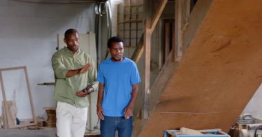 İş birliği yapan Afrikalı Amerikalı meslektaşlar atölyedeki tableti inceliyor, ahşap tahtaları inceliyor. Sanatçılık, takım çalışması, sanayi, inşaat, yenilik, kırsal, üretkenlik