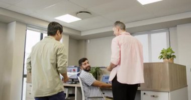 Muhtelif iş arkadaşları ofis masasındaki monitörlerdeki çizelgeleri inceleyip belgeleri değiş tokuş ediyor ve tableti tıkırdatıyor. İşbirliği, takım çalışması, veri analizi, iş toplantısı, ofis ortamı, dijital teknoloji, profesyonel tartışma