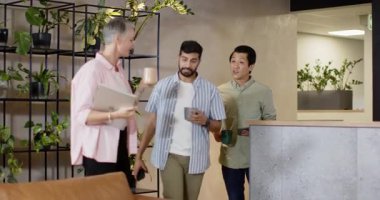 Karşılıklı selamlaşmalar bitkilerin yanından geçip kanepede diz üstü bilgisayarla iş birliği yapan çeşitli iş arkadaşları. İşbirliği, takım çalışması, modern, çalışma alanı, ağ oluşturma, iletişim, gelişigüzel