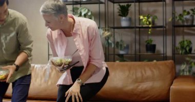 Çeşitli arkadaşlar salata kabı taşıyarak içeri giriyor, kapakları açıyor ve kahverengi kanepede öğle yemeğini paylaşıyorlar. Gündelik, sosyal, sağlıklı, iletişim, rahatlama, modern, konfor