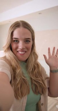 Dikey video: Seyirciyi selamlamak, yatak odasında kadın filmi çekmek, seyirciyi selamlamak için el sallamak. Portre, günlük, neşeli, yaşam tarzı, samimi, samimi, dikey video