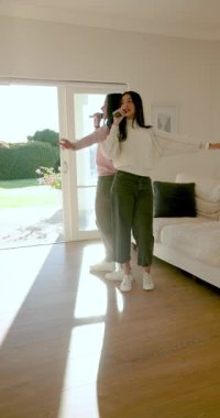 Aydınlatılmış oturma odasında şarkı söyleyen ve dans eden çeşitli bayan arkadaşlar mikrofonları gösteriyorlar. Konser, performans, düet, kutlama, uyum, koreografi, dikey video