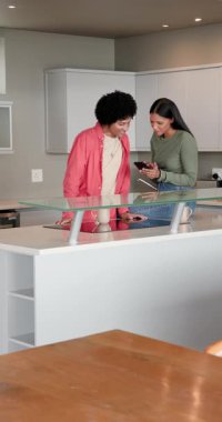 Mutfak adasındaki çeşitli bayan arkadaşlar telefon sürprizini paylaşıyor ve yemek pişirmek için ürünleri açıyor. Arkadaşlık, işbirliği, gündelik, modern, yaşam tarzı, sağlık, dikey video