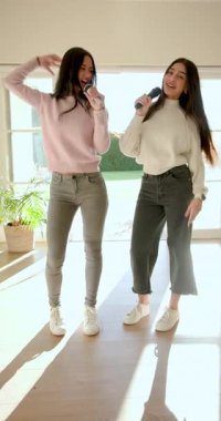 Çeşitli bayan arkadaşlar ellerinde kablosuz mikrofonlarla düet yapıp cam kapının yanında sallanıyorlar. Canlı, neşeli, dostluk, uyum, performans, gündelik, dikey video