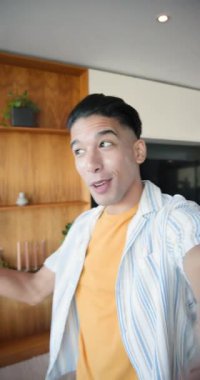 Dikey video: Erkek yaratıcı kamerayı selamlıyor akıllı telefonu evde rafları ve sandalyeleri gösteriyor. Yaşam tarzı, iç mekan, minimalist, modern, ev, gündelik, dikey video