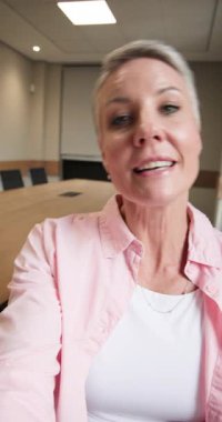 Dikey video: 50 'li yaşlarda bir kadın akıllı telefon kaydına başlıyor, konuşuyor ve başını masaya çeviriyor. Profesyonel, iletişim, sunum, samimi, modern, özenli, dikey video