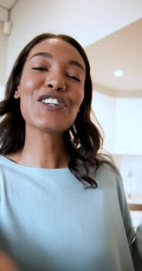 Dikey video: Mutfakta kameraya gülümseyen ve lense mesaj yollayan bir kadın. Portre, yaşam tarzı, samimi, neşeli, iç mekan, sıradan, dikey video