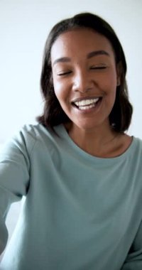 Dikey video: Yatakta el sallayan ve telefona konuşan Afro-Amerikalı kadın vlogger görüntüsü giriliyor. Portre, yaşam tarzı, samimi, modern, doğal, anlamlı, dikey video