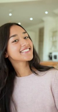 Dikey video: Kulağının arkasında saçlar, mutfakta izleyicileri selamlamak için gülümseyen ve üfleyen bir kadın. Zarif, neşeli, yaşam tarzı, güzellik, rahat, rahat, dikey video